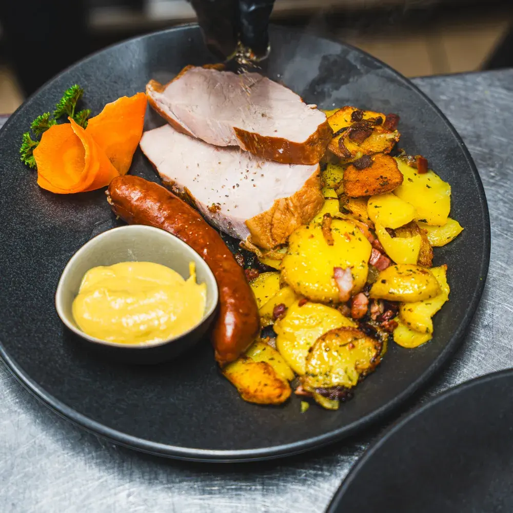 Kassler wird auf den Teller zu Kohlwurst, Bratkartoffeln und Senf gelegt