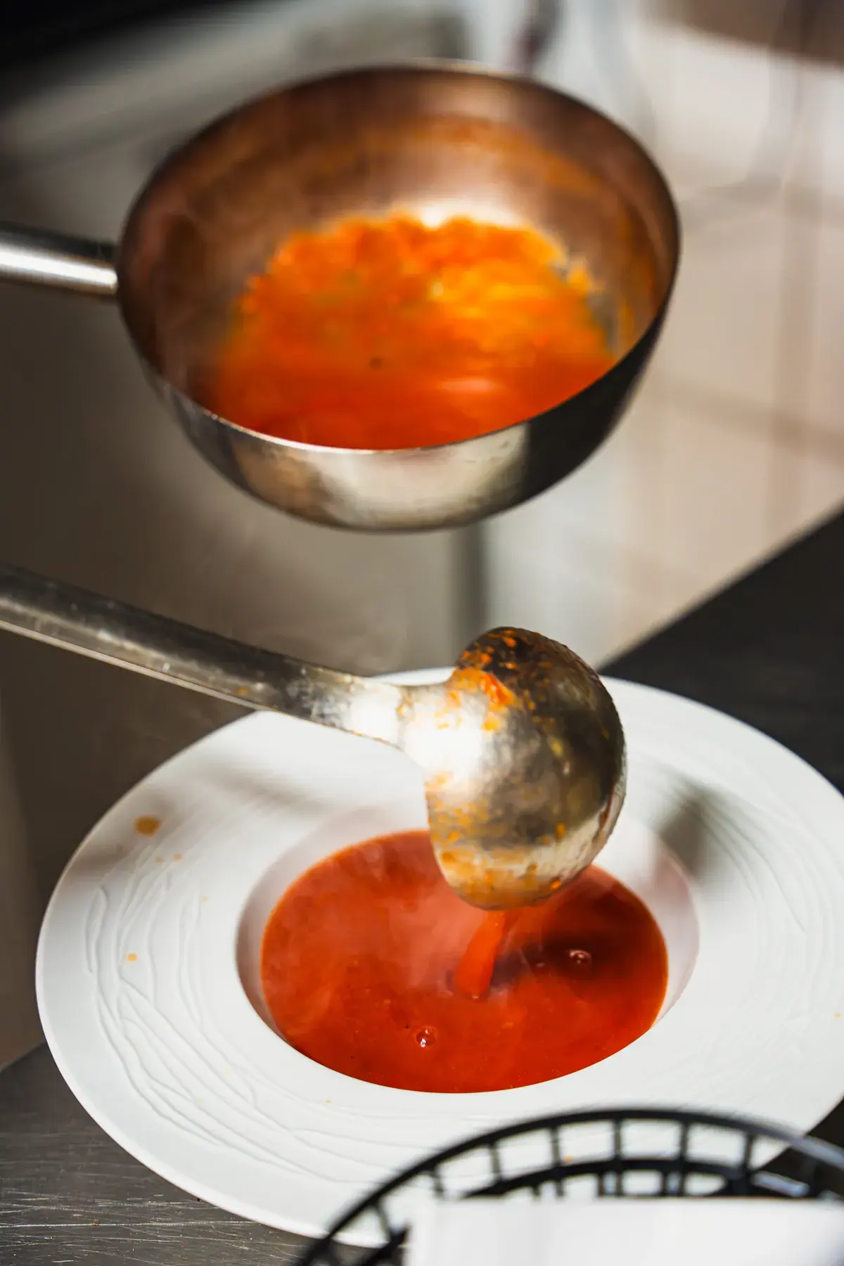 Tomatensuppe wird mit der Kelle in einen tiefen Teller gegeben