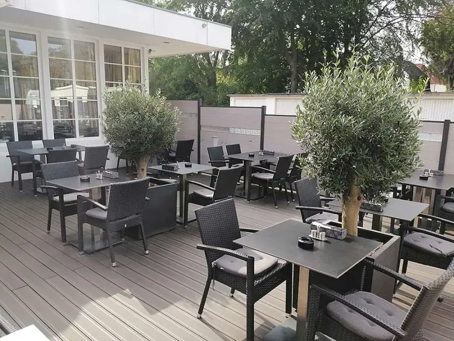 Die Terrasse mit Holzdielen, Korbstühlen und Olivenbäumen in Kübeln